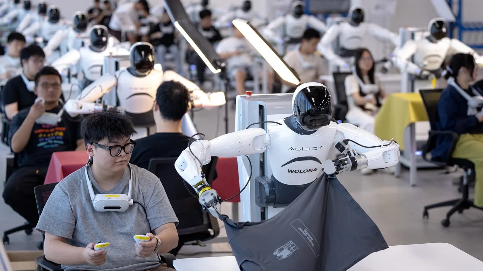 Rader av humanoida robotar på en teleoperationsträningsgolv, med operatörer vid varje station.